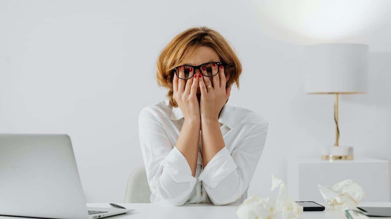 A stressed woman covering her face while sitting at a desk.