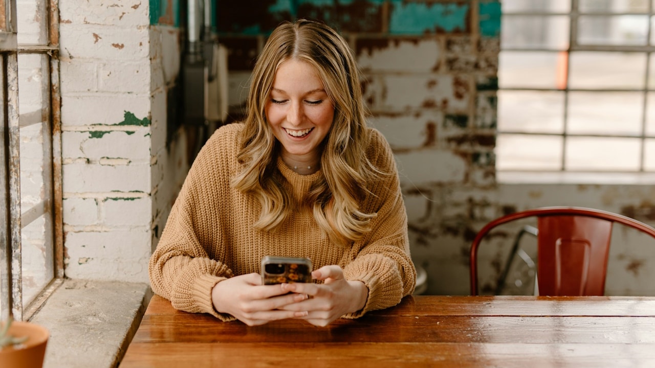 A woman texting and smiling while sitting at a table.