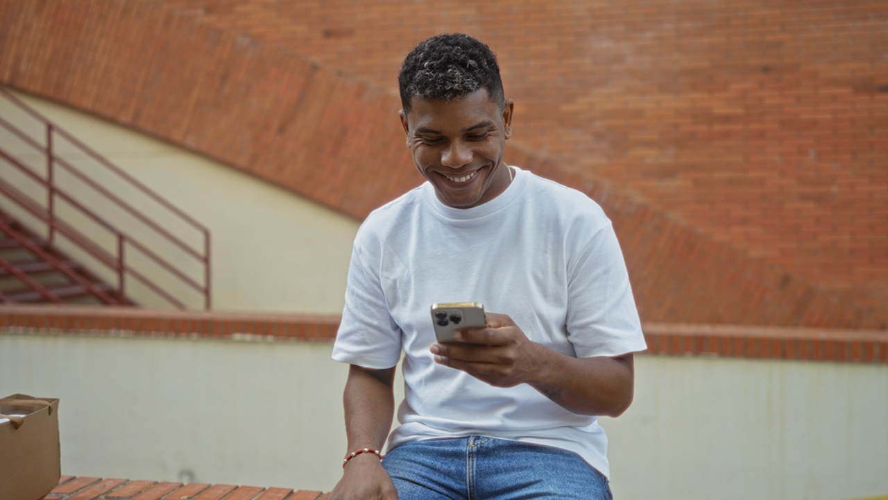 A smiling man in a white t-shirt and jeans using his smartphone outdoors.