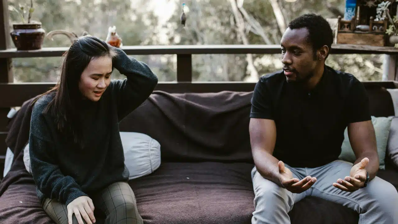 A man and woman sitting on an outdoor sofa, gesturing during an intense conversation together.