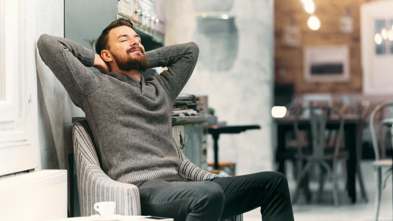 A man in a gray sweater leans back in a chair with his eyes closed.