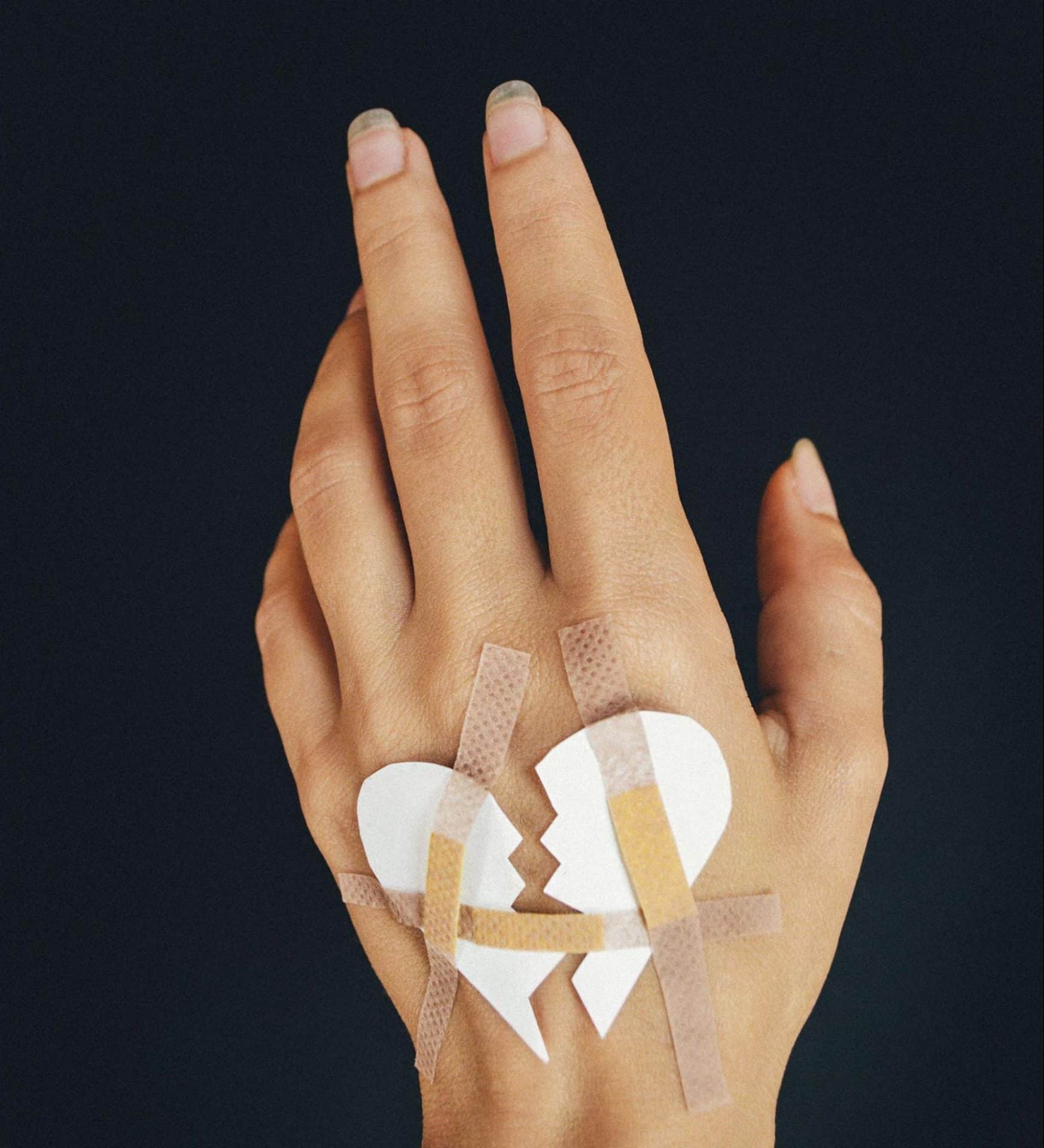 A hand with a broken heart cut out pasted on it.