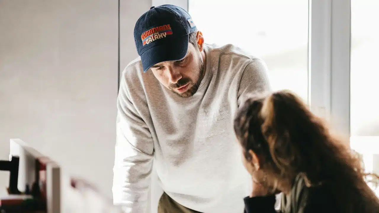 A man wearing a baseball cap leans down to talk with a woman.