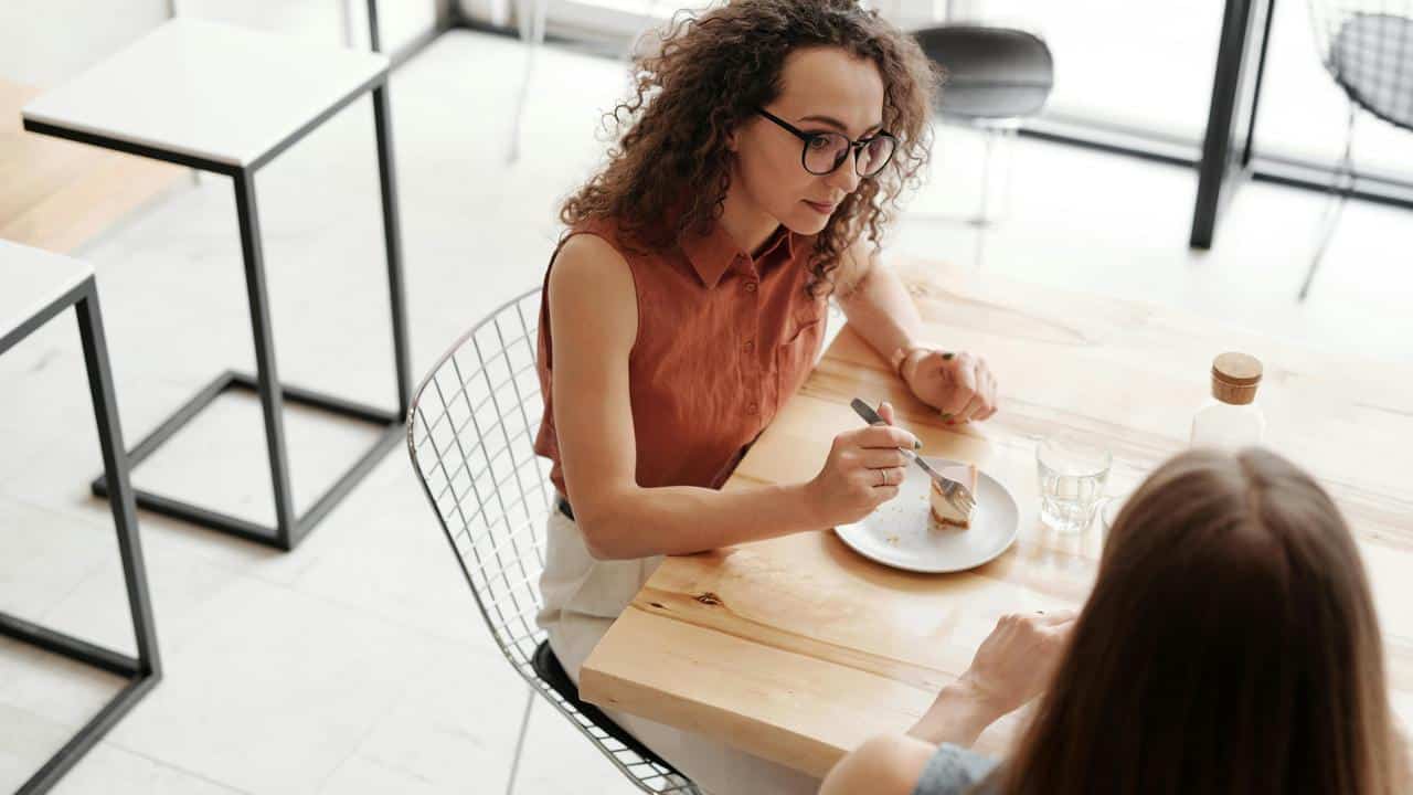 A woman talking while eating dessert at a table with another person.