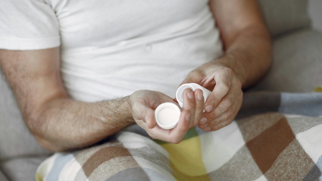 Close-up of a person's hands holding an open white pill bottle and a plastic cap.