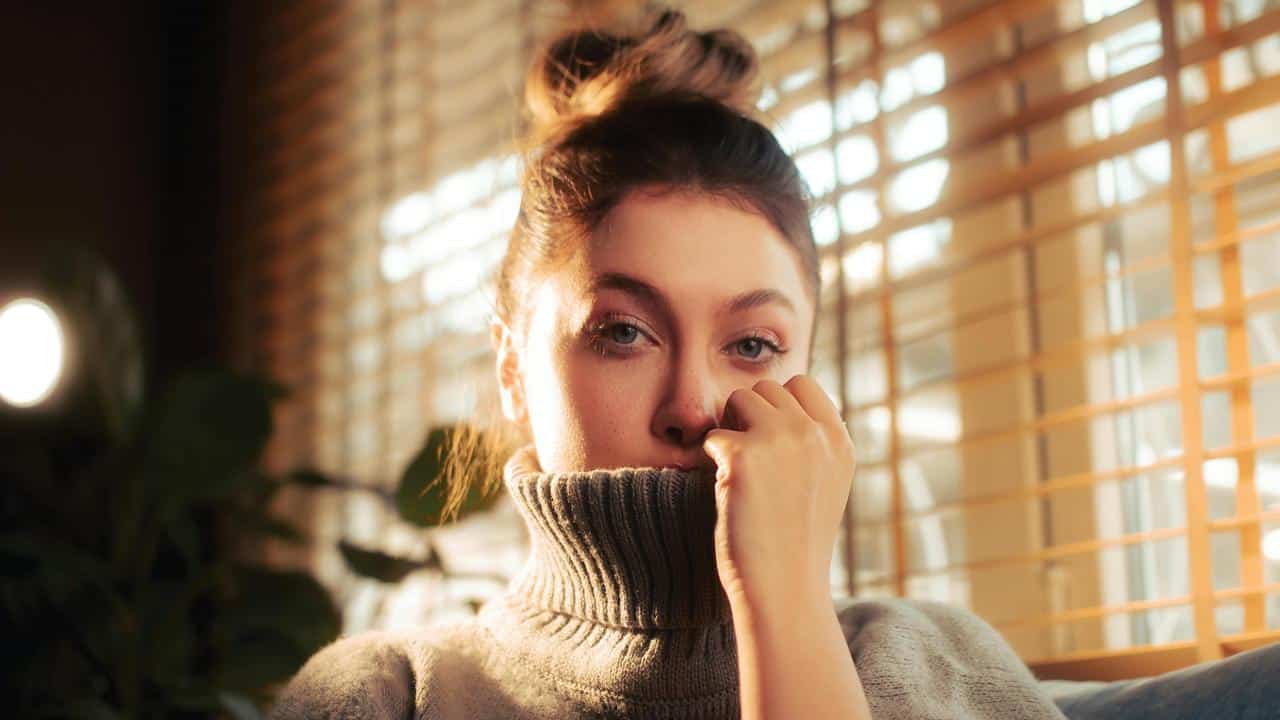 A woman looking thoughtful while sitting by a window.