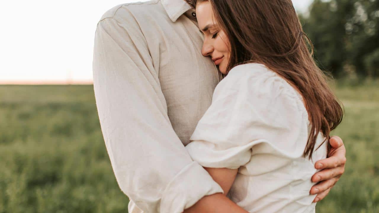 A woman hugging a man outdoors with her eyes closed.