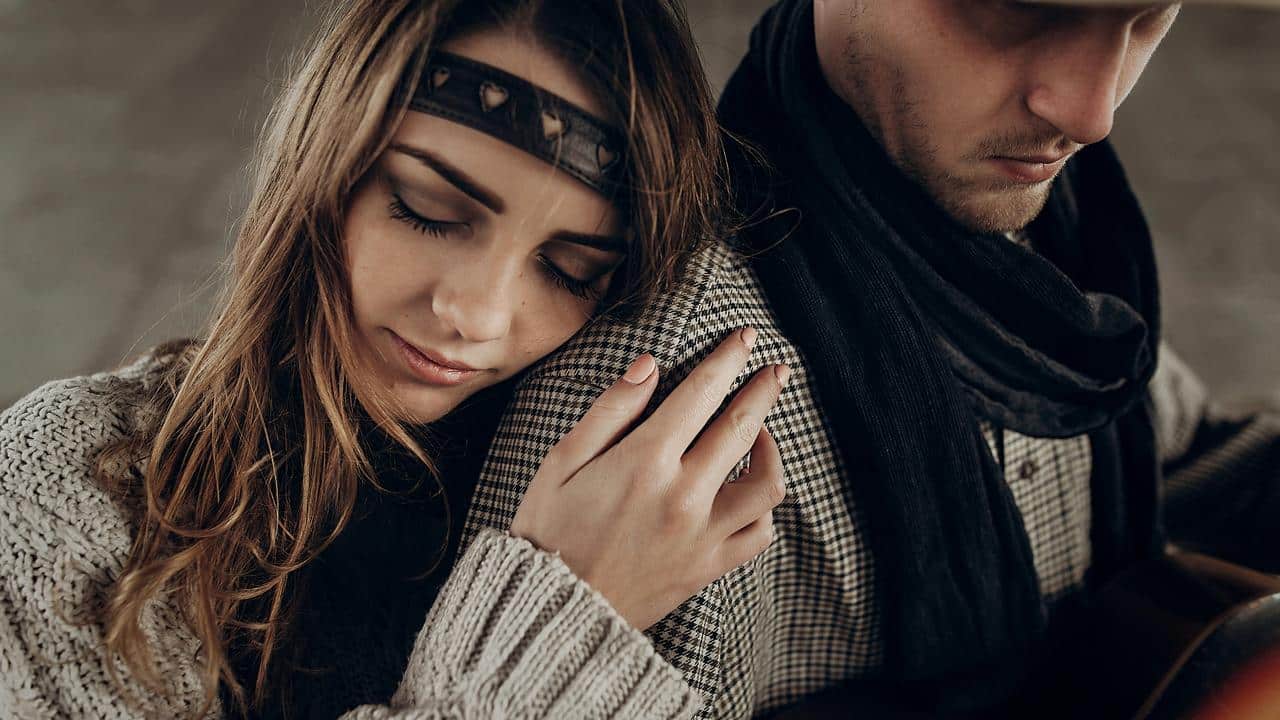 A woman resting her head on a man's shoulder as they sit together.