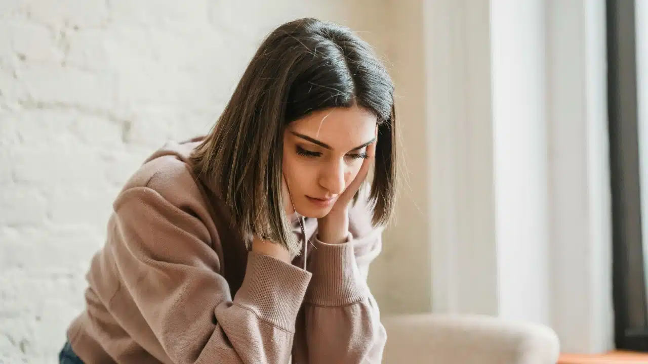 A woman in a mauve hoodie sits with her chin resting in both of her hands.