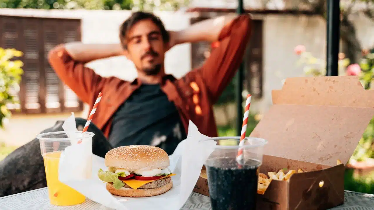 A hamburger and fries sit on a table in front of a blurry seated man.