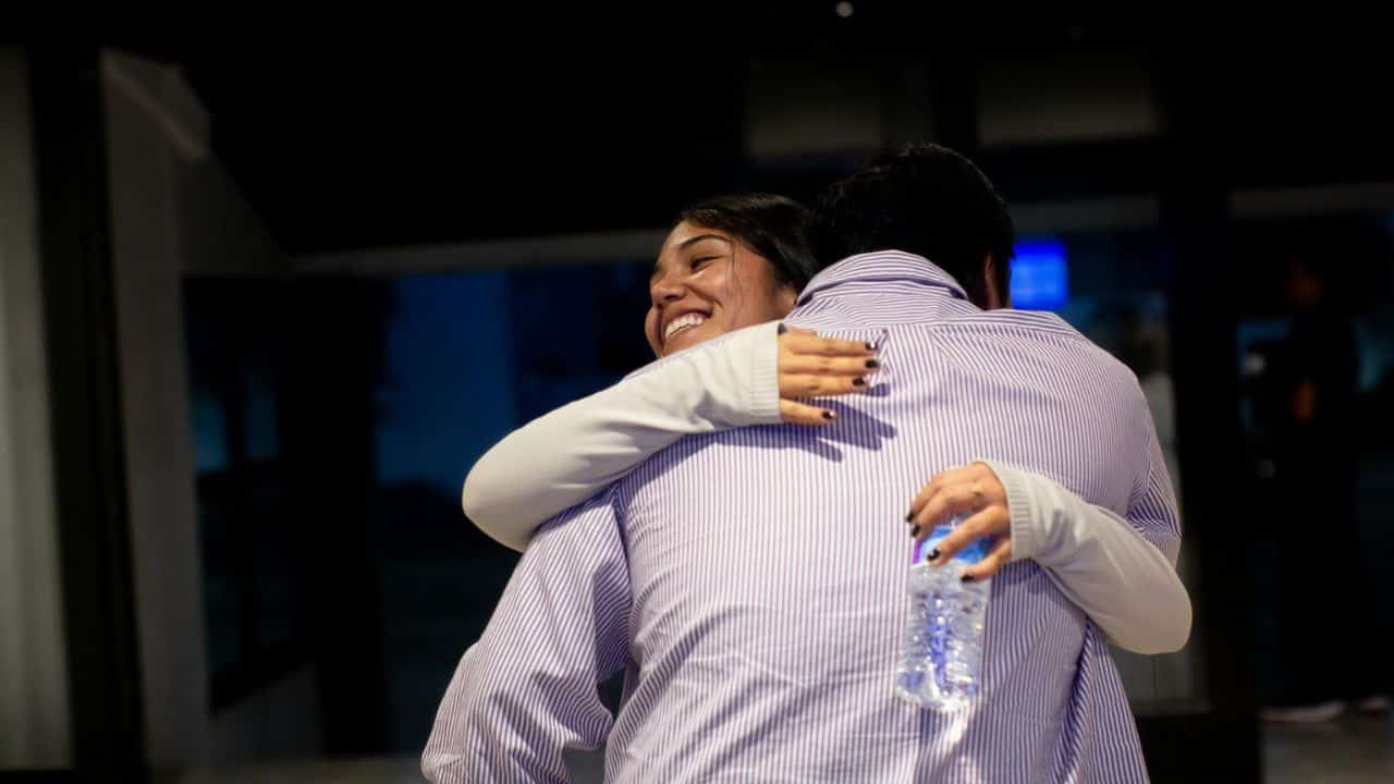 A smiling woman embraces a man, holding a water bottle.