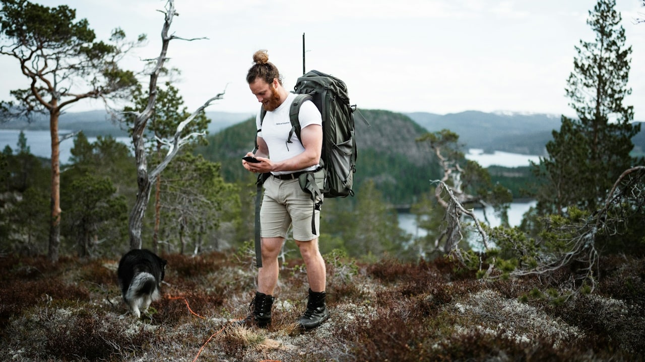 A person with a backpack and a dog on a trail by a lake.