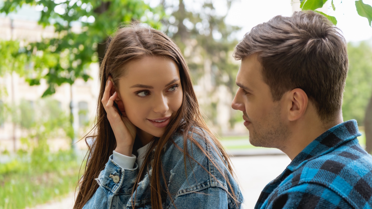 A young couple looking at each other outdoors, the woman in a denim jacket.