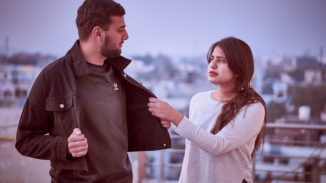 A woman grabbing her husband's jacket while they are standing on a rooftop.