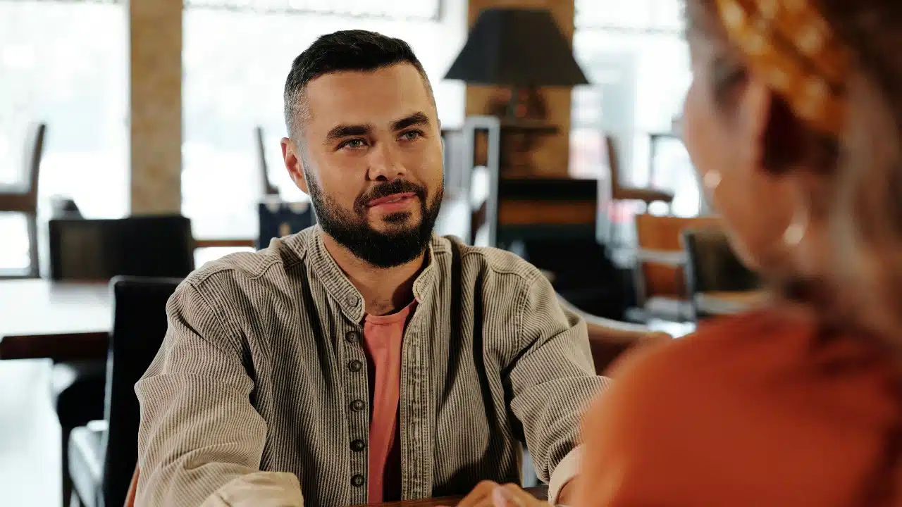 A bearded man in a striped shirt looking toward a person in the blurred foreground.