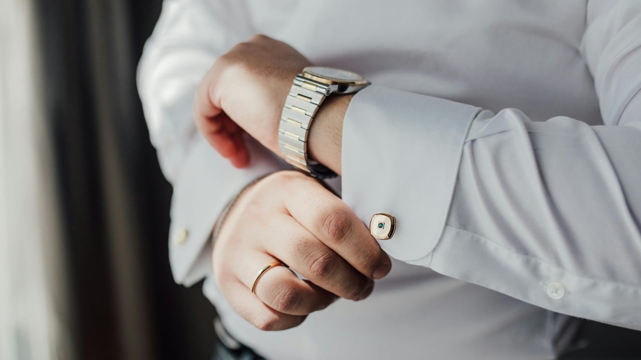 A person in a white dress shirt adjusts a gold cufflink on their sleeve.
