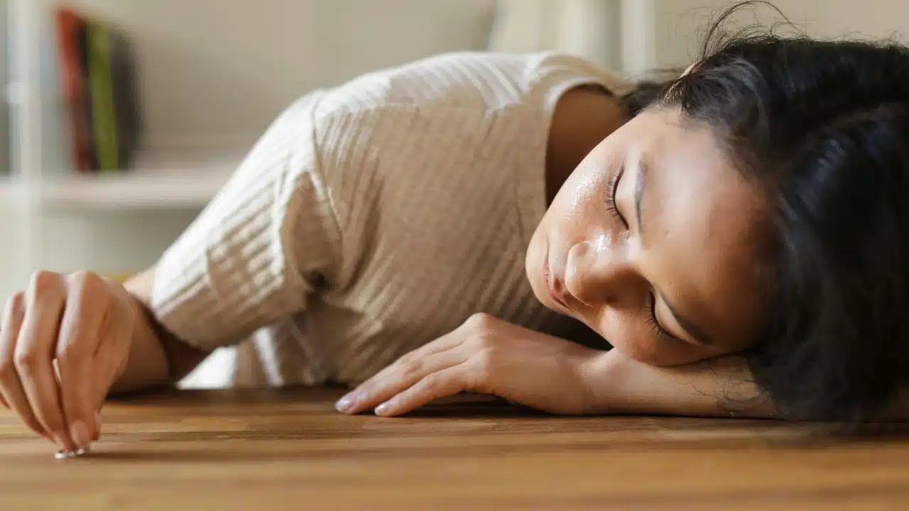 A woman rests her head on a wooden table with a single ring placed nearby.