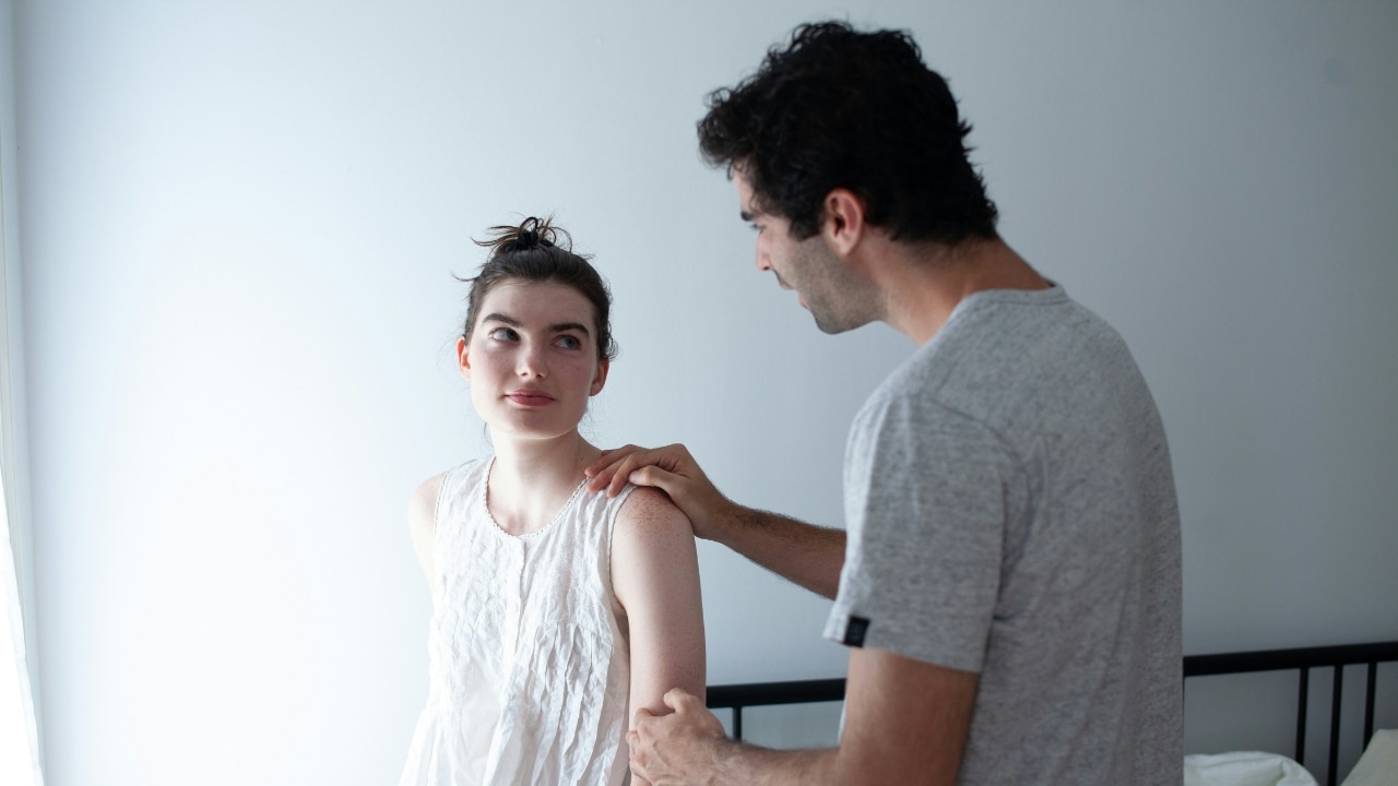 A man places his hand on the shoulder of a woman who is looking upward.