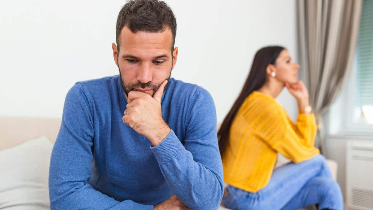 A man sits with his hand on his chin while a woman sits behind him.