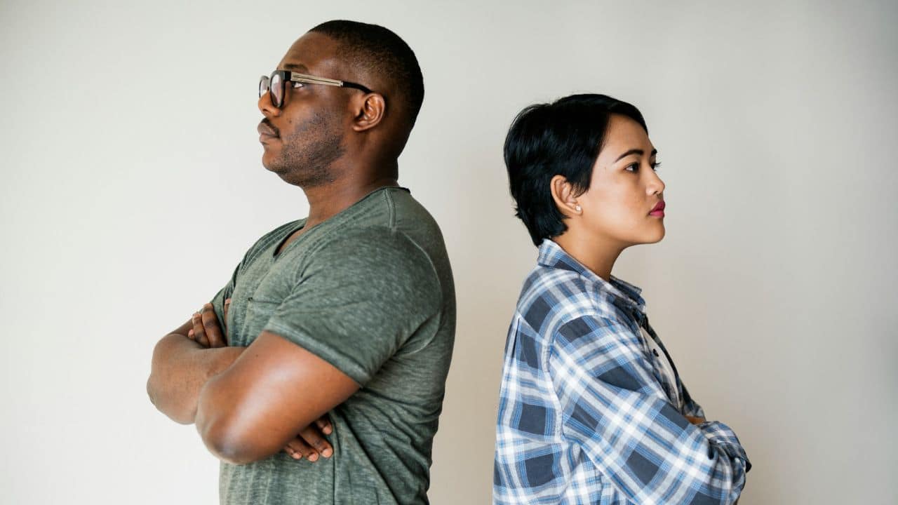 A man and woman stand back-to-back with arms crossed against a white background.
