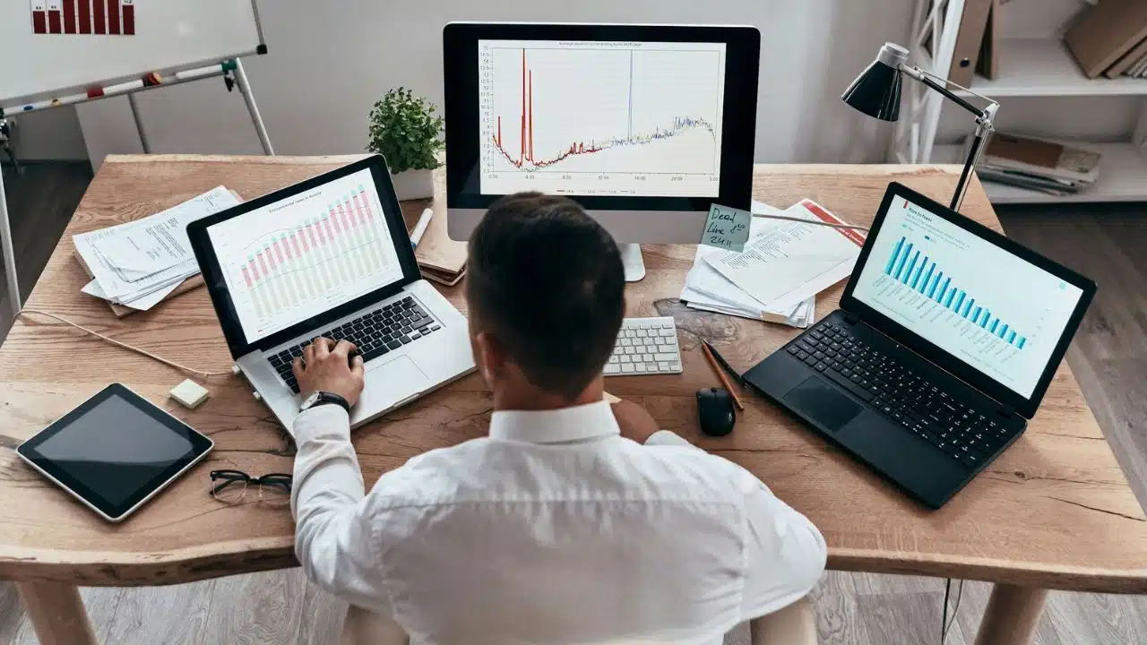 High-angle view of a man at a desk working with multiple monitors displaying various financial graphs.
