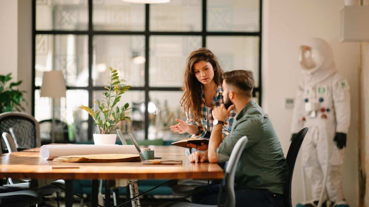 A woman talking to a man with concern while working together at a desk