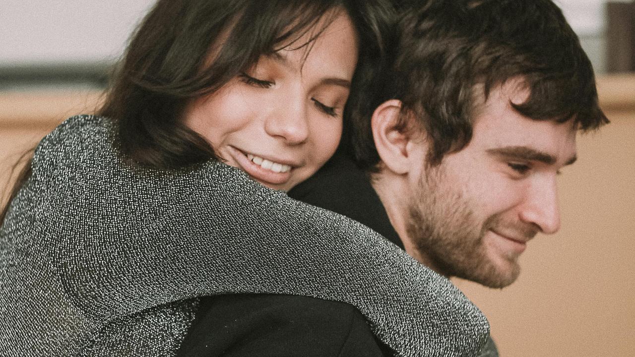 A woman hugging a man from behind with her eyes closed and smiling.
