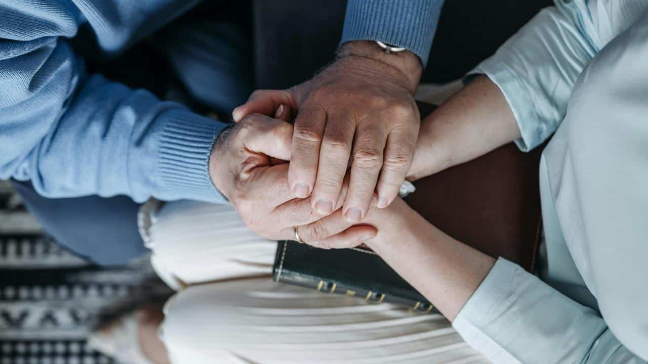 A close-up of two people gently holding hands in a comforting gesture.