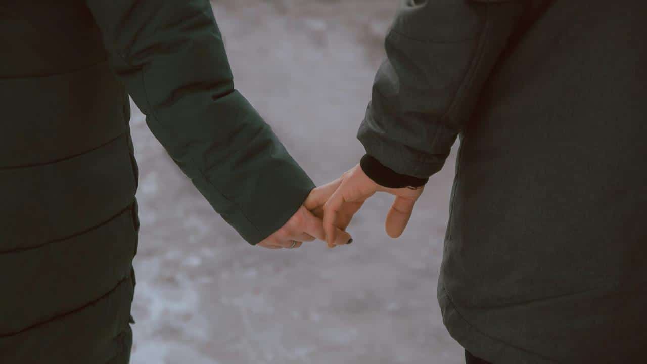 A couple holds hands while walking together in winter coats.
