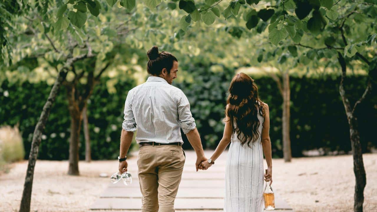 A couple holding hands and walking together through a tree-lined path.