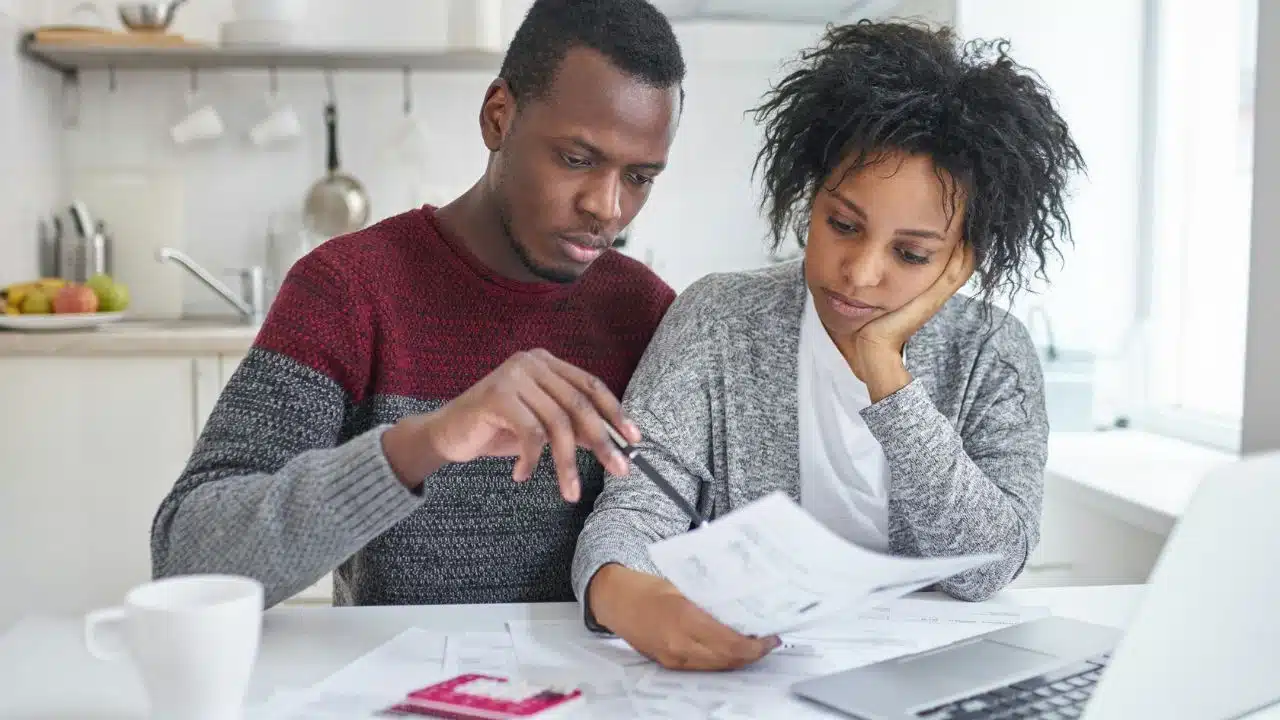 A man and woman sit at a table reviewing paperwork and looking at a laptop.
