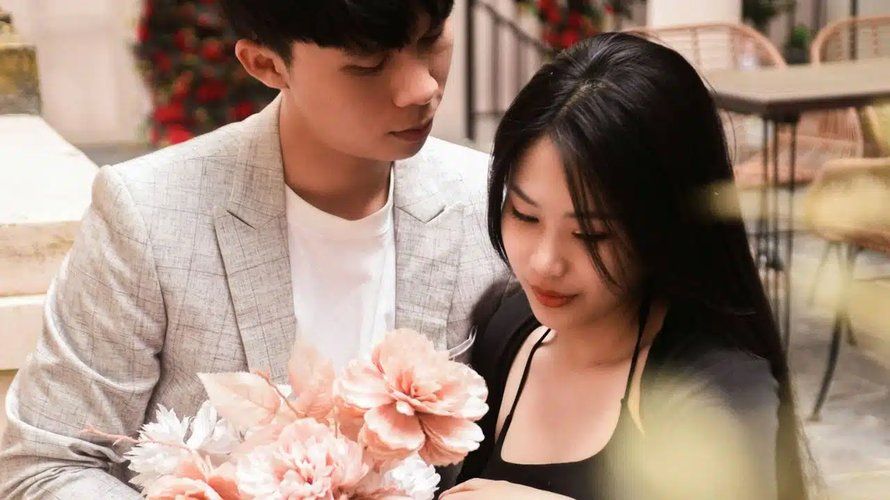 A man in a light blazer looks down at a woman holding a pink bouquet.