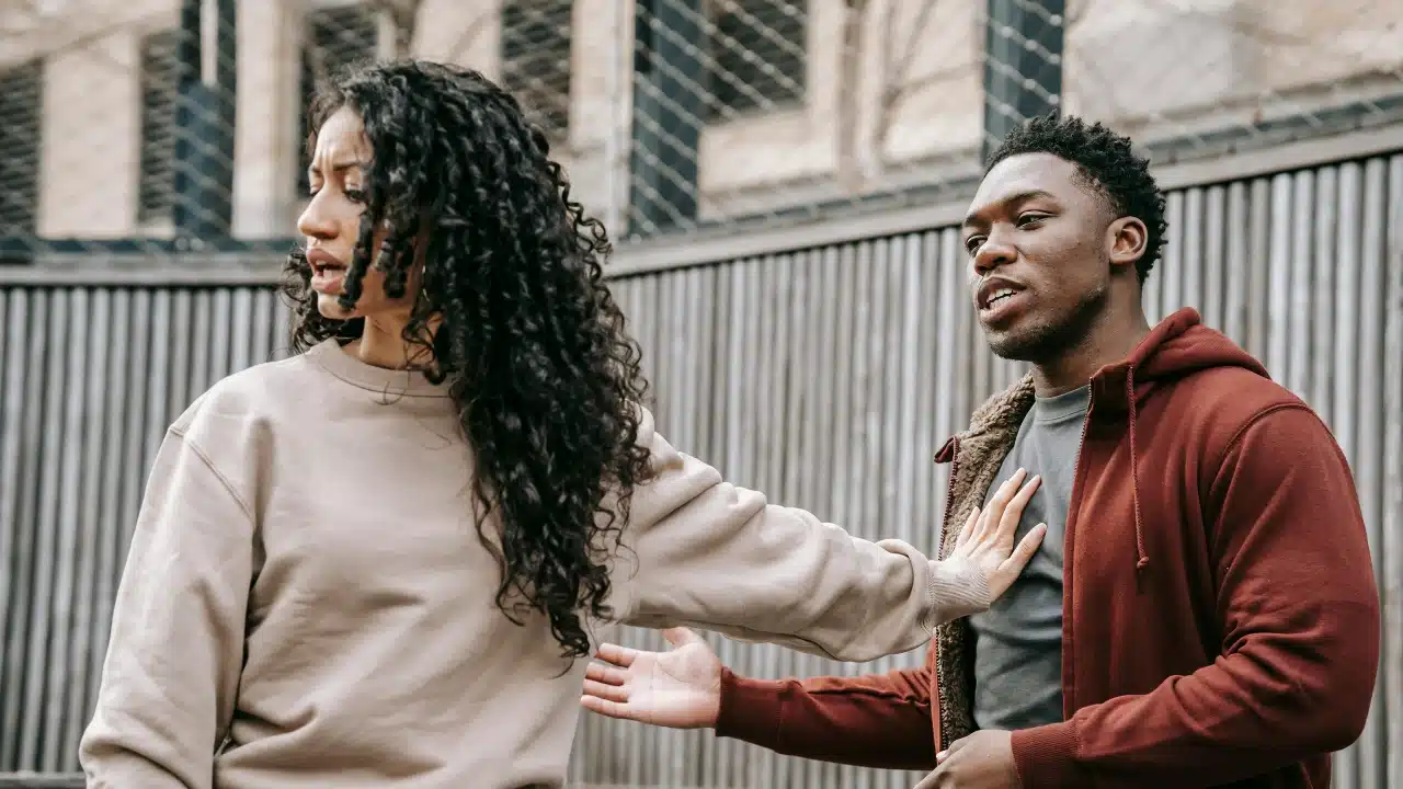 A woman with curly hair extending her hand toward a man wearing a red hoodie.