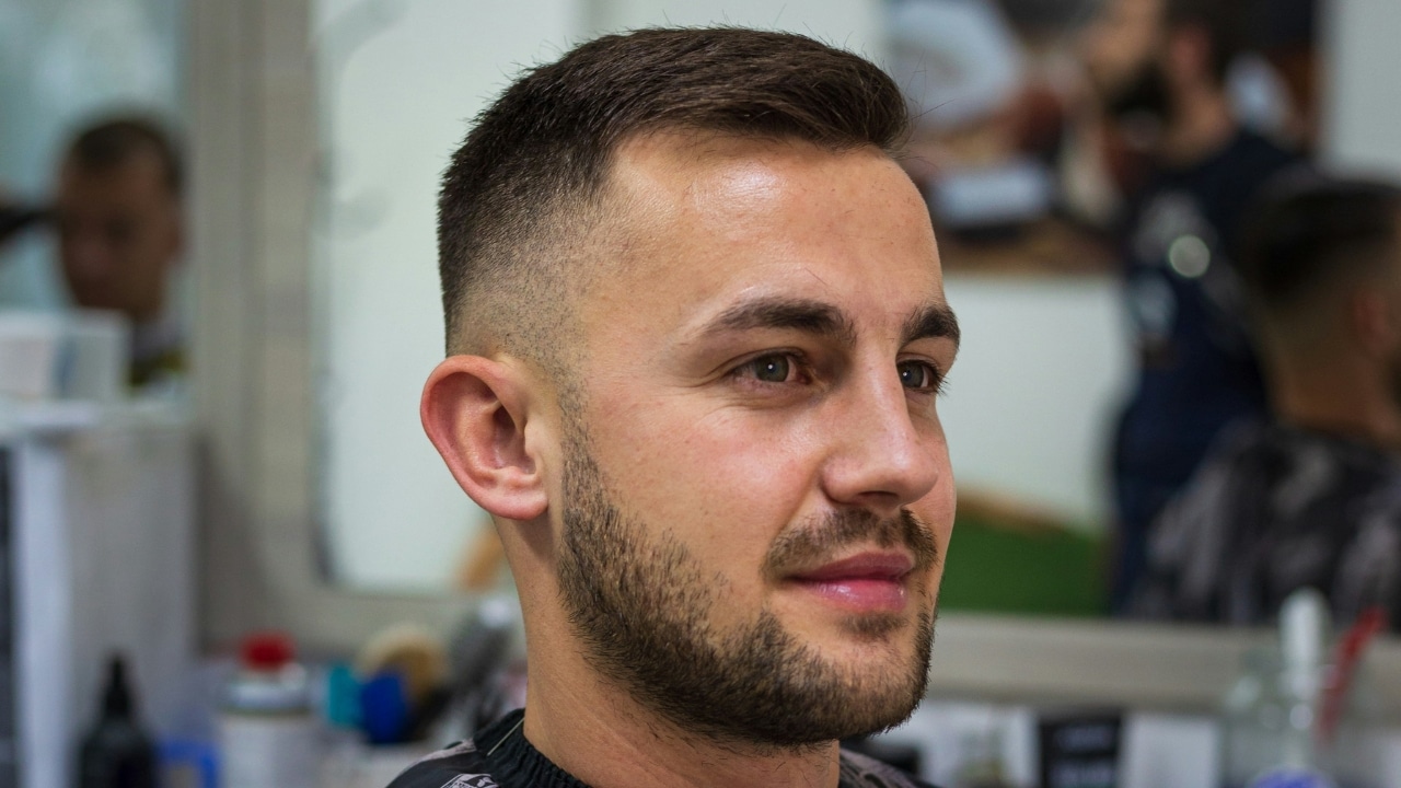 A close-up profile of a man with a faded haircut and a neatly trimmed beard.