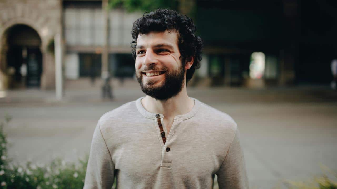 A smiling man standing outdoors, looking off to the side.