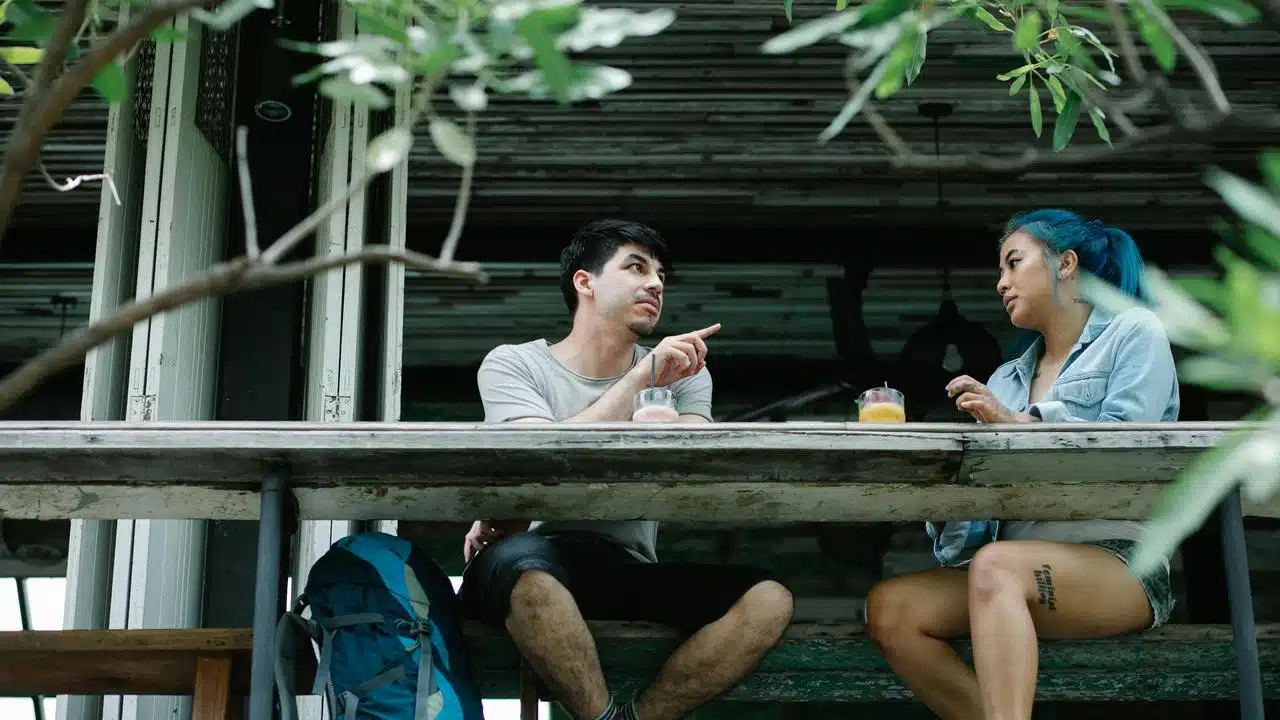 A man and woman talking at an outdoor table with drinks.