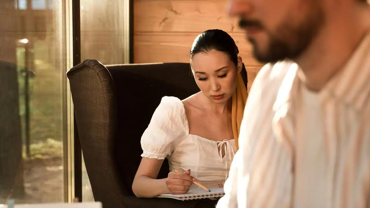 A woman writing in a notebook while sitting beside a man.
