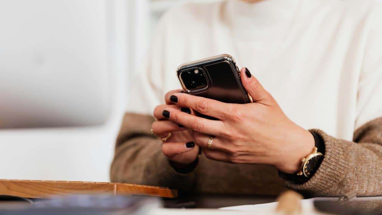 A woman holding a smartphone while sitting at a desk.