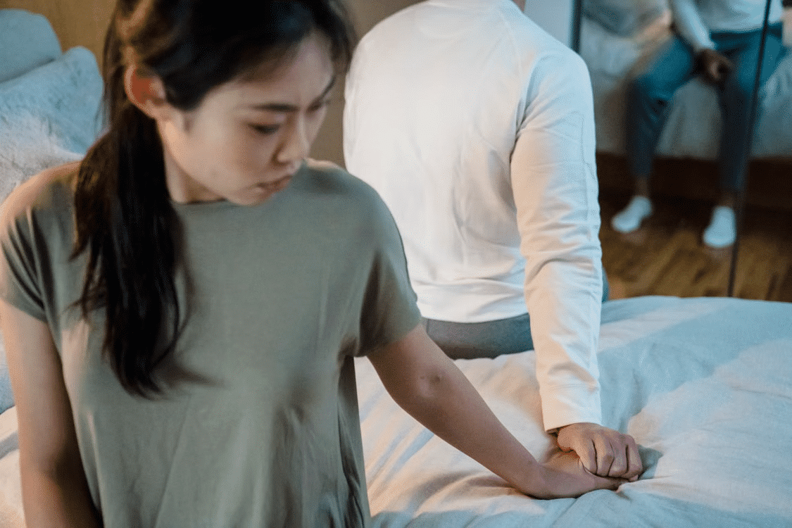 A woman seems uninterested in intimacy as a man gently presses her hand.