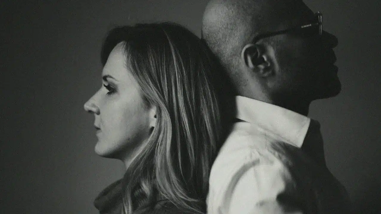 A black and white profile photo of a woman and man leaning back to back.