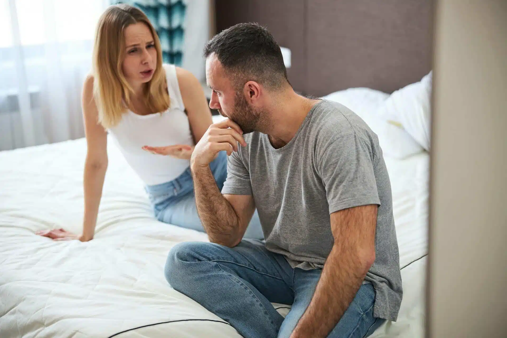 A woman complaining to a man who looks vacuous while they sit on a bed.