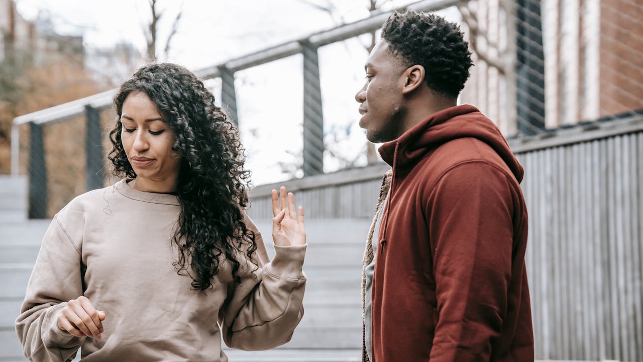 A woman putting up her hand to stop or refuse an interaction with a man standing nearby.