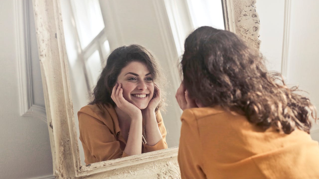 A self-contented woman looking in a mirror and smiling.