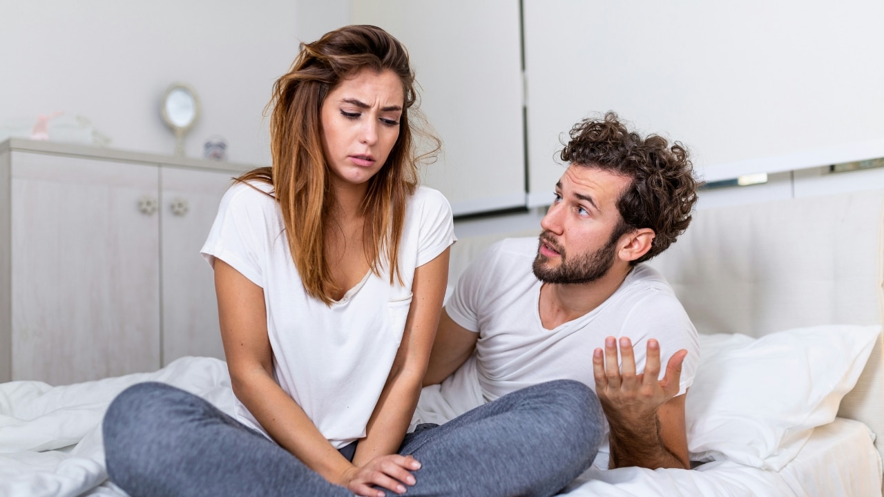 A man with curly hair talks and gestures while a woman looks away from him.