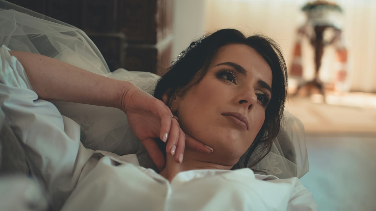 A woman with dark hair leans back against white fabric and looks toward the side.