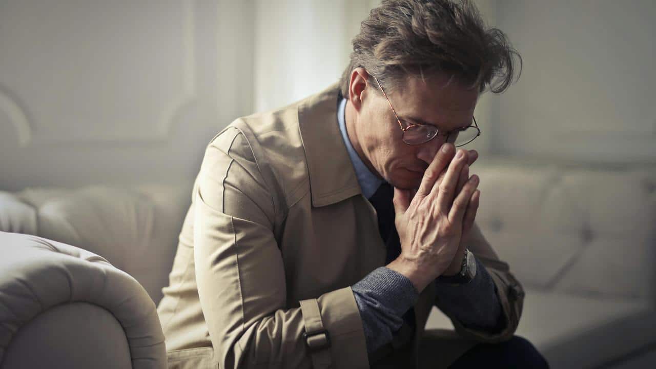 A man sitting with hands clasped, looking stressed.