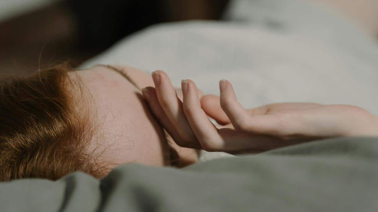 A curly-haired person resting their head on a hand by a window.