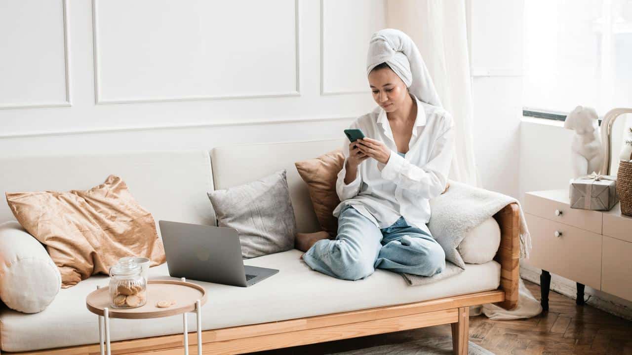 A woman with a towel on her head sitting on a couch and using her phone.