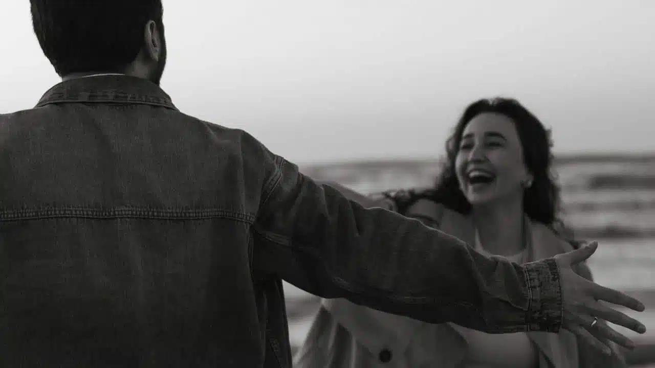 A man with open hands standing in front of a laughing woman who is coming towards him.