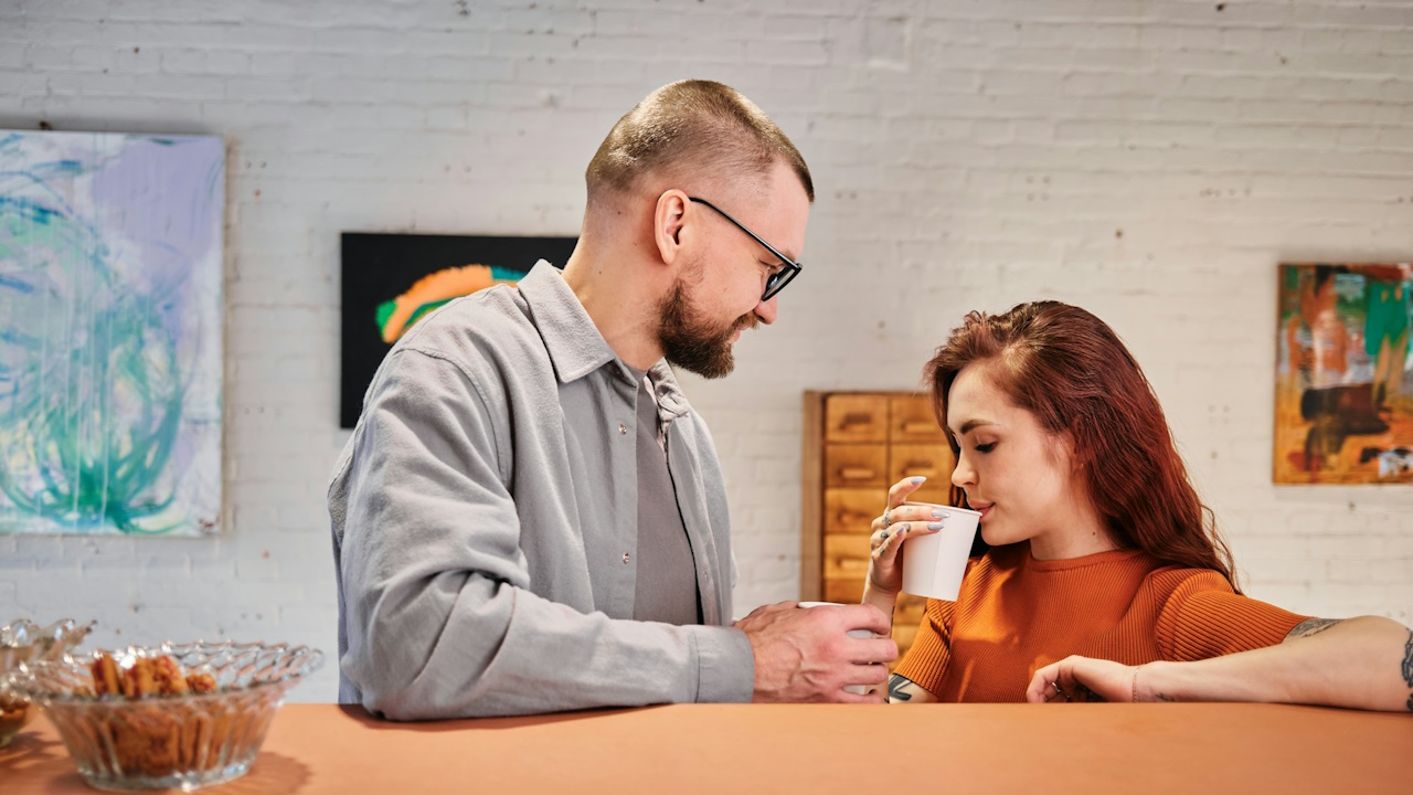 A man and woman standing next to each other holding cups of coffee.